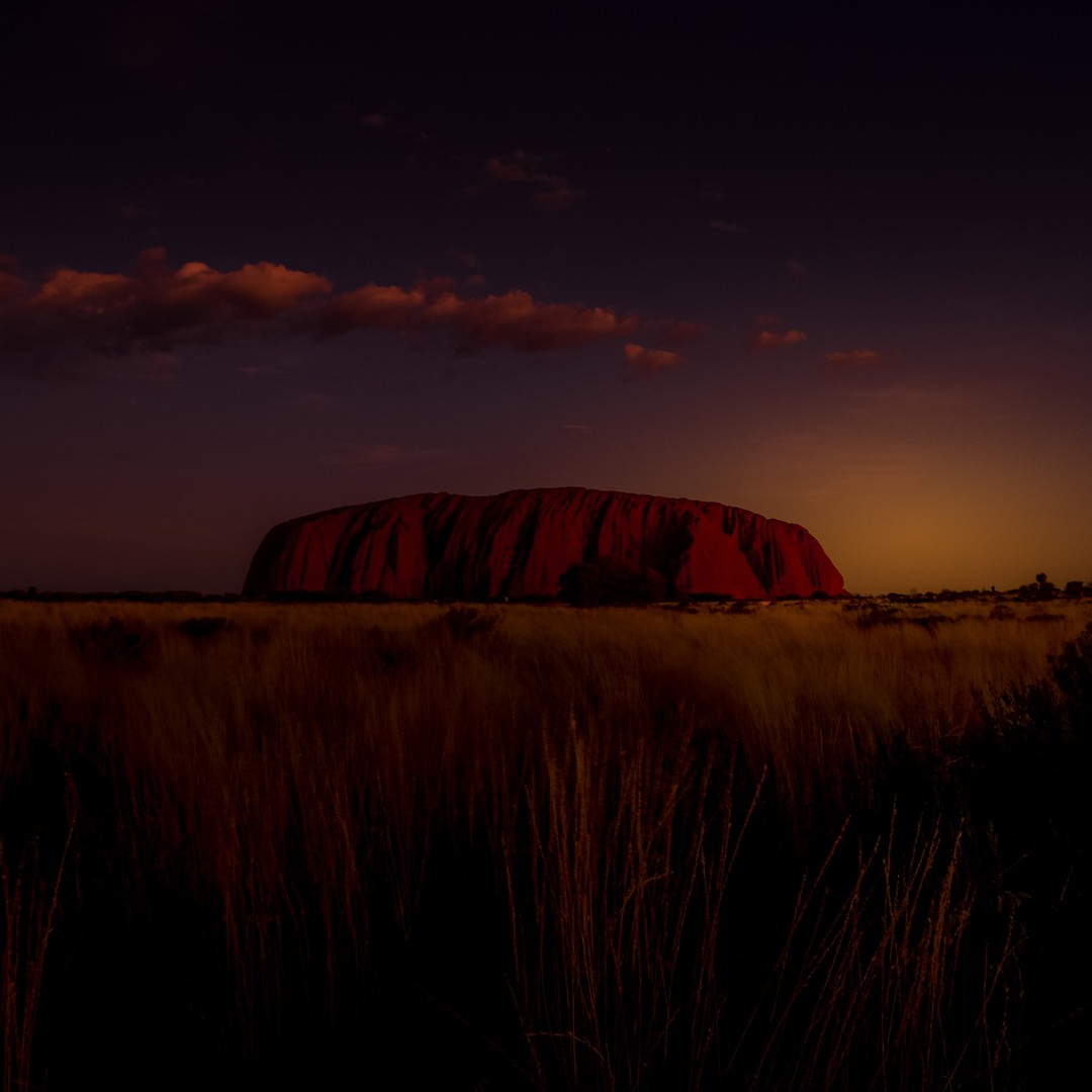 Watching the sunset at #Uluru in @australia. The hulking clay-red monolith is arguably the most famous sight in all of Oceania. We watched the sun-scorched sentry slowly change colour for what felt like an age. It was time well spent. ⁣
⁣
Uluru lives up to the hype. It looms long and heavy, and is unavoidably affecting. In walking around its base, one almost feels a presence: a formidable, sombre presence, as if Uluru were placed there by design and not just accident. It’s silly we know, but that is how we felt.⠀ ⁣
⁣
Here was the rock we had seen in movies, postcards and documentaries, a rock that symbolised past conflict and enduring pain, a rock held sacred by Australia’s indigenous people.⁣
-⠀⠀⁣
-⠀⠀⁣
-⠀⠀⁣
-⠀⠀⁣
-⠀⠀⁣
-⠀⠀⁣
#Australia #seeaustralia  #exploreuluru #ayersrock #ulurukatatjutanationalpark  #ulurusunset  #visitaustralia #northernterritory  #ntaustralia #katatjuta #alicesprings #theoutback #outbackaustralia  #lpPathfinders #redcentre