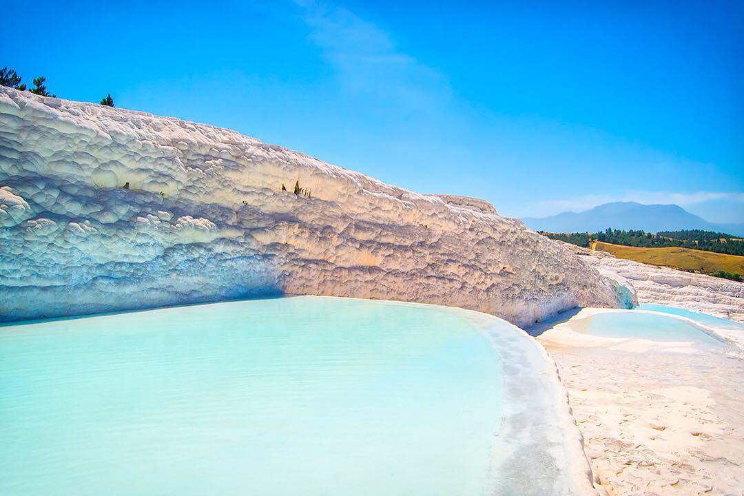 Sweeping limestone cliffs of a blinding white hue rise above layered pools of powder blue at the terraces of Pamukkale in Turkey.⠀⠀
⠀⠀
Pamukkale’s surreal landscape was formed over millennia by limestone deposited by 17 hot springs in the area. Sadly, its natural beauty was almost lost when hotels sprung up around the area in the 1960s and a road was built to allow motorbikes direct access over the slopes! The hotels drained the thermal waters to fill their swimming pools and the terraces turned a greyish brown.⠀⠀
⠀⠀
Thankfully, in 1988, UNESCO stepped in and declared Pamukkale a World Heritage Site. The hotels were demolished and a series of artificial pools built atop the road to hide the damage caused. ⠀
⠀
Today, there are strict controls on development and tourism in the area, allowing you to visit in good conscience.⠀⠀
⠀⠀
#Pamukkale #Turkey #Denizli #travel #Hierapolis #betabookings #Kusadasi #spirit #HomeOfHealth #body #travelgram #wanderlust #vacation #instatravel #view #travelphotography